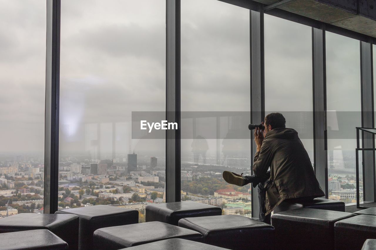 Man looking at cityscape through binoculars while sitting at office