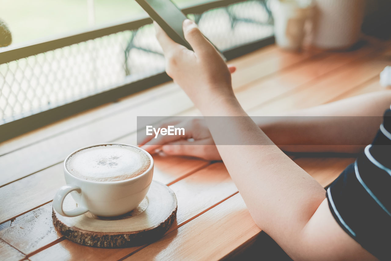 Cropped image of woman using mobile phone by coffee on table