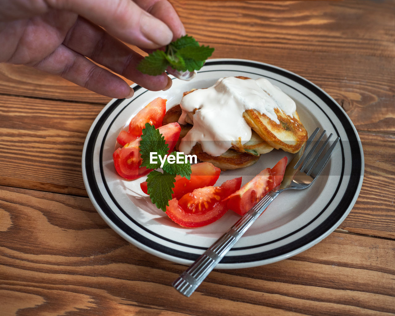 A female hand lays a sprig of mint on a pancake house. pancakes with sour cream on a wooden table