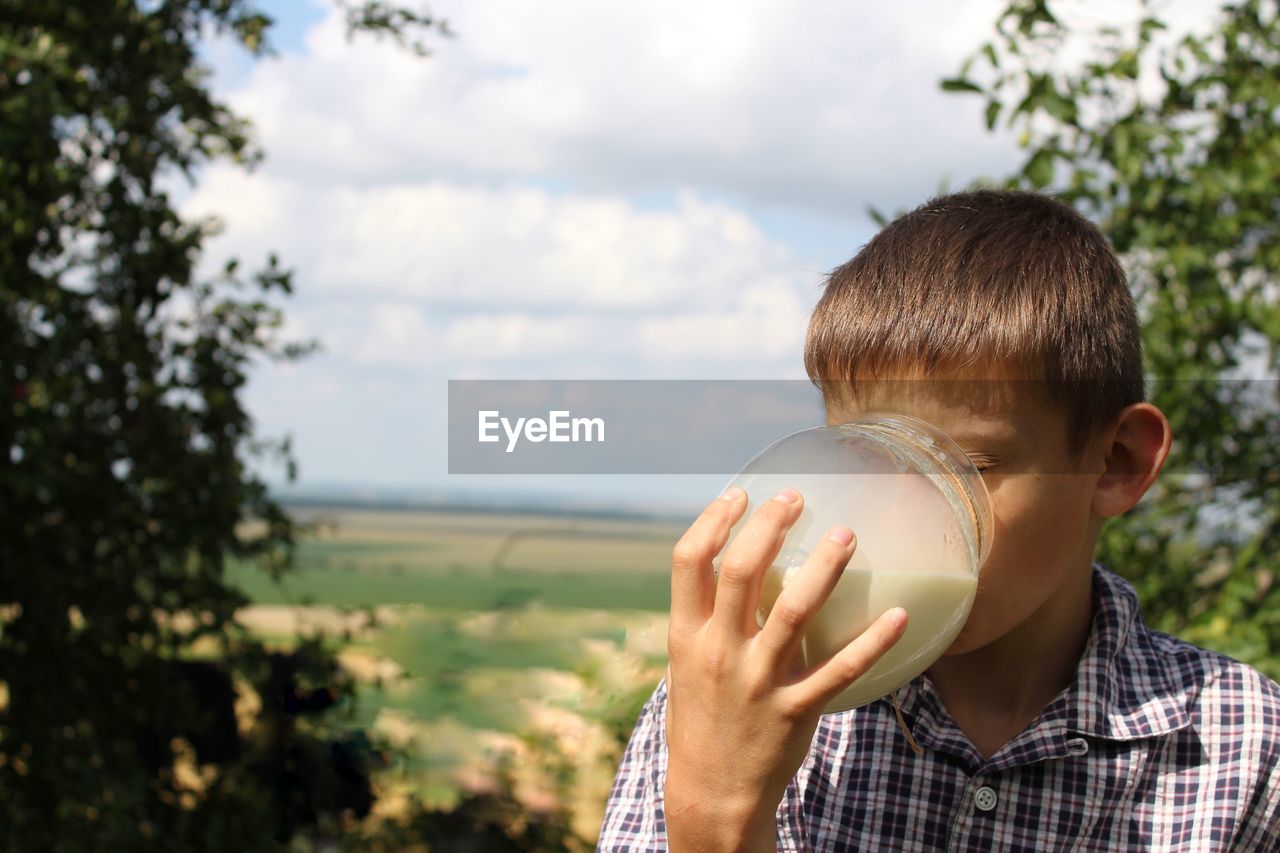 A boy in a checkered shirt enjoys fresh milk in the village in the summer