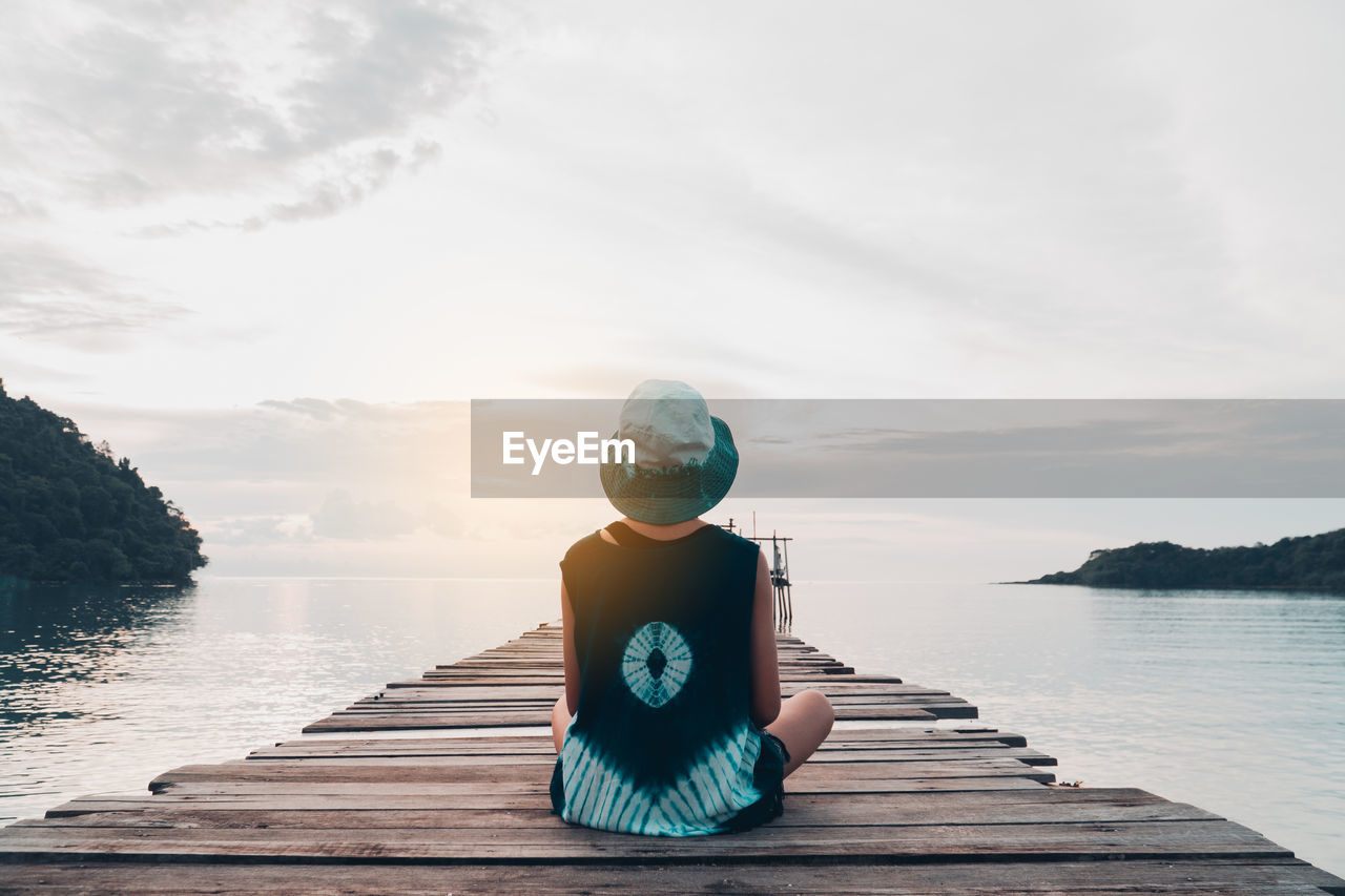 MAN SITTING ON PIER AGAINST LAKE