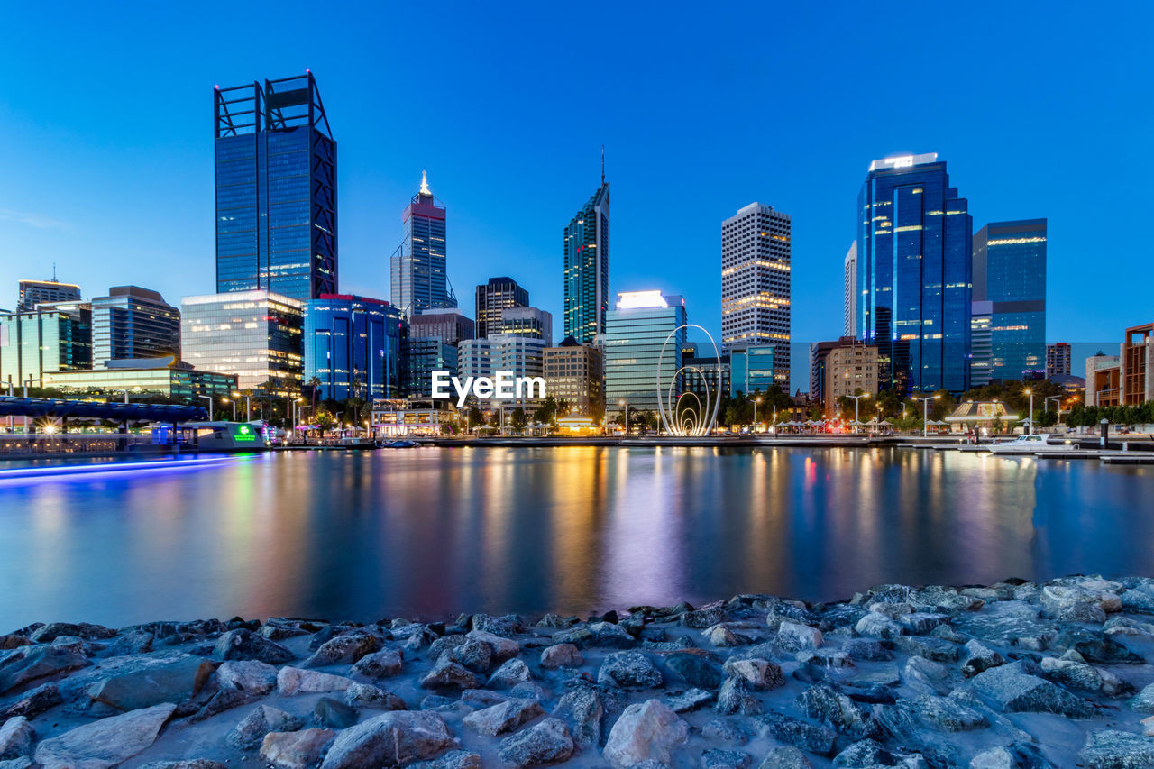 Sea by illuminated buildings against blue sky