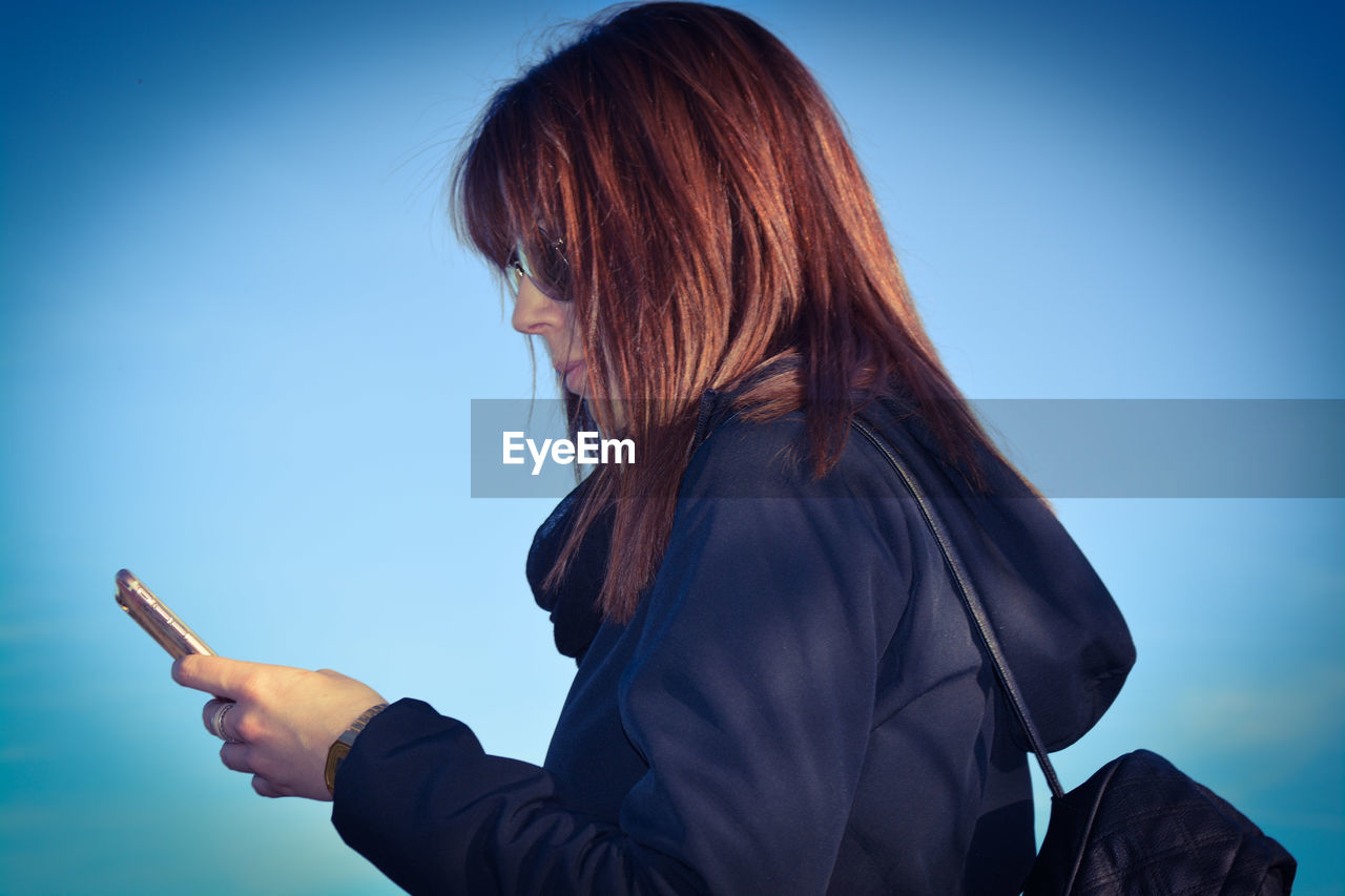 Side view of woman using phone against sky