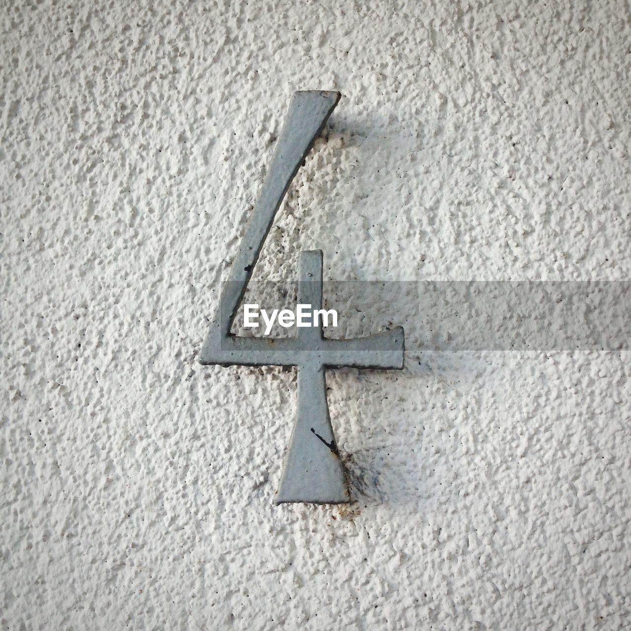Close-up of rusty metallic number 4 on rough white wall