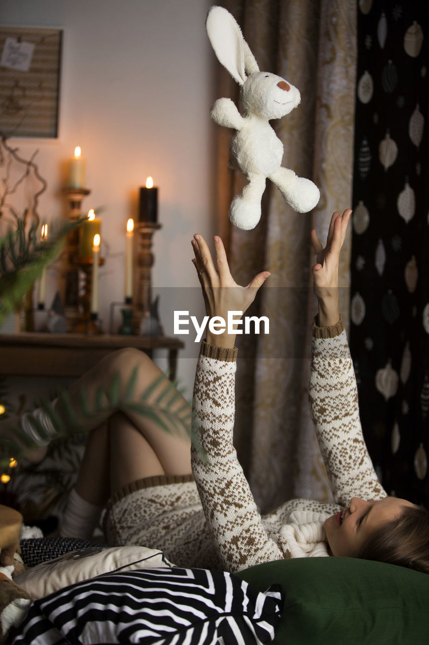 Mid adult woman playing with stuffed toy while lying on bed at home