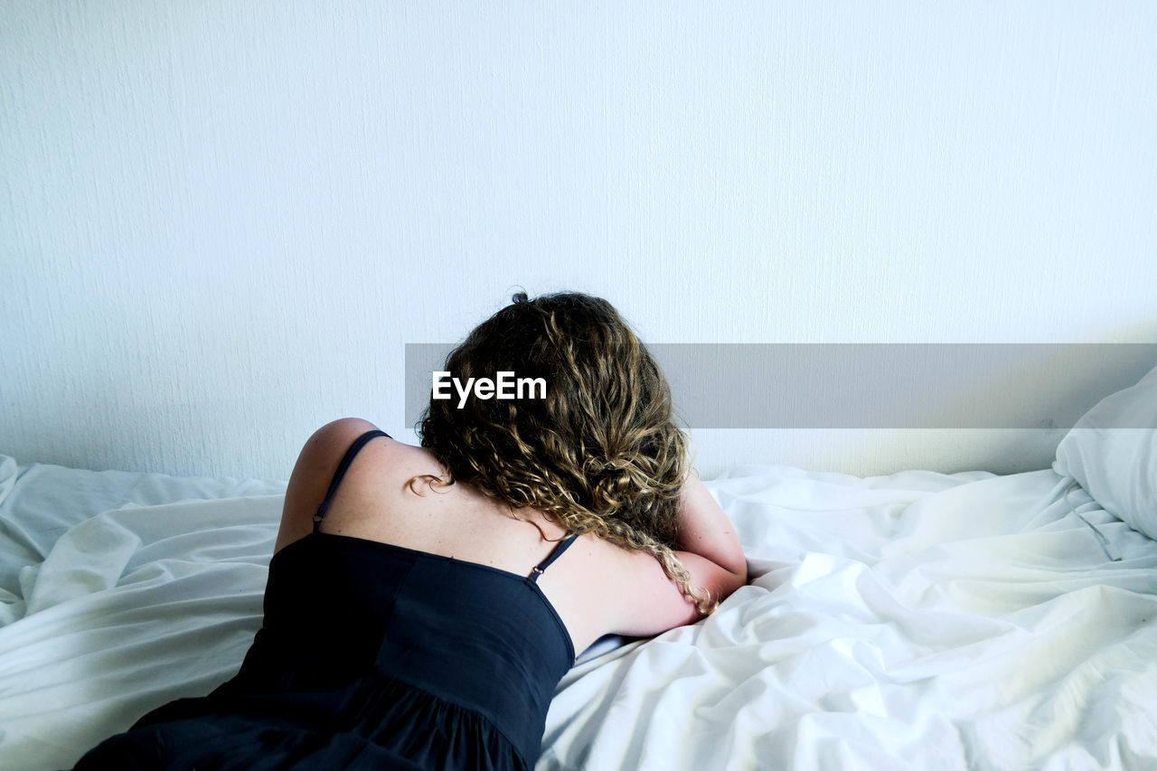 Rear view of young woman lying on bed at home