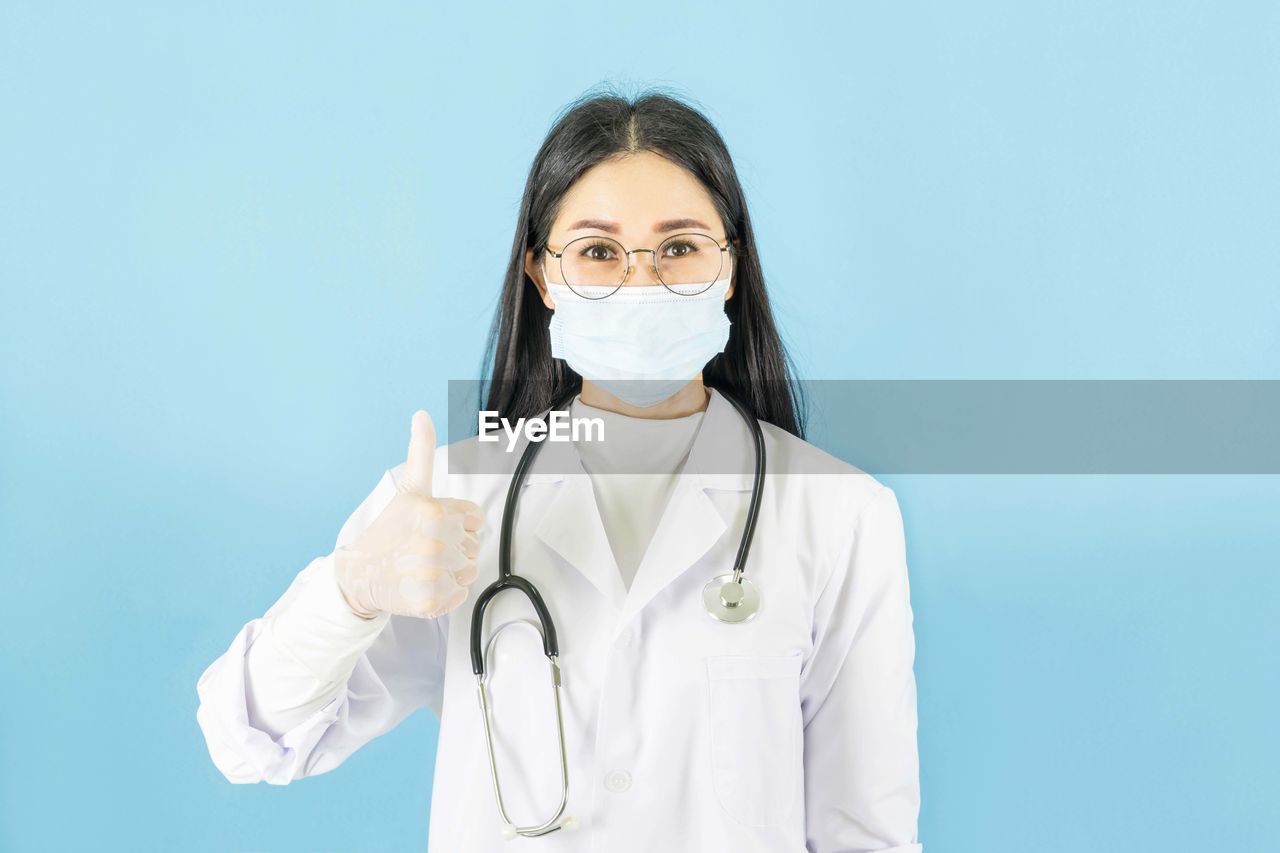 Portrait of doctor showing thumbs up against blue background