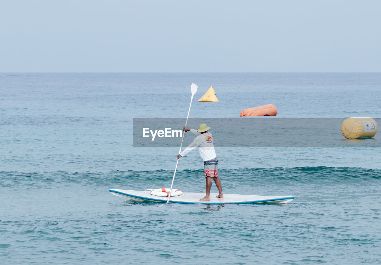 Man paddleboarding in sea against clear sky