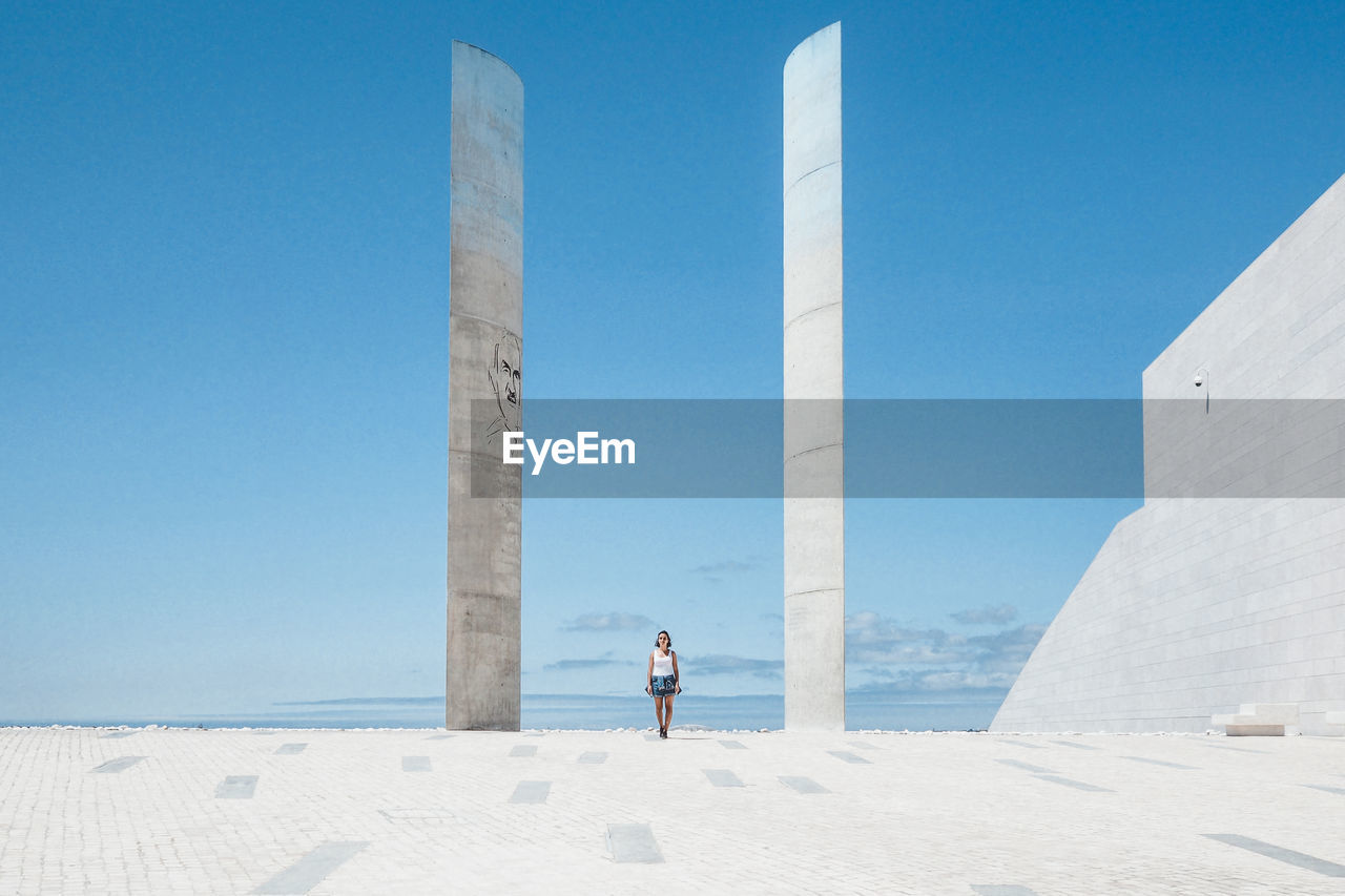 Young woman standing at monument against blue sky