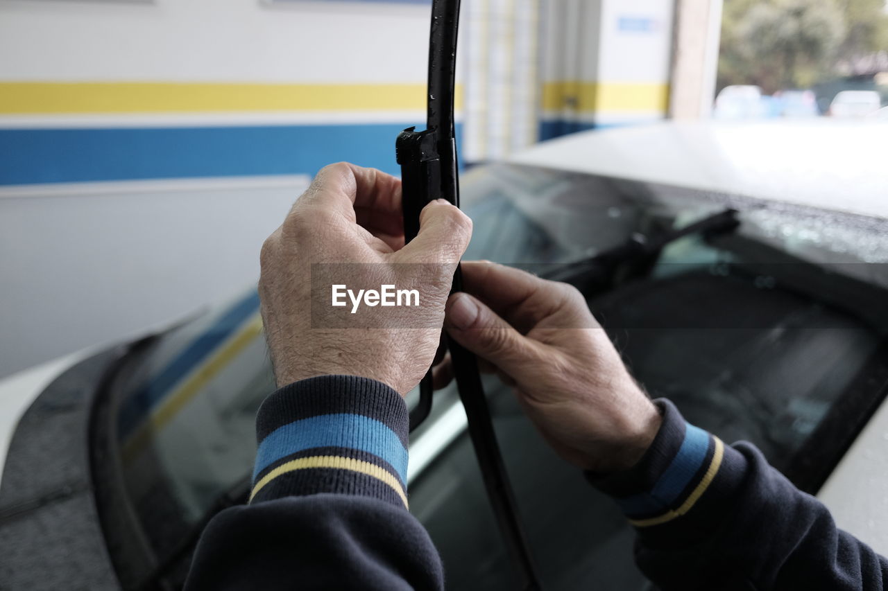 Cropped hands of mechanic holding windshield wiper against car at auto repair shop