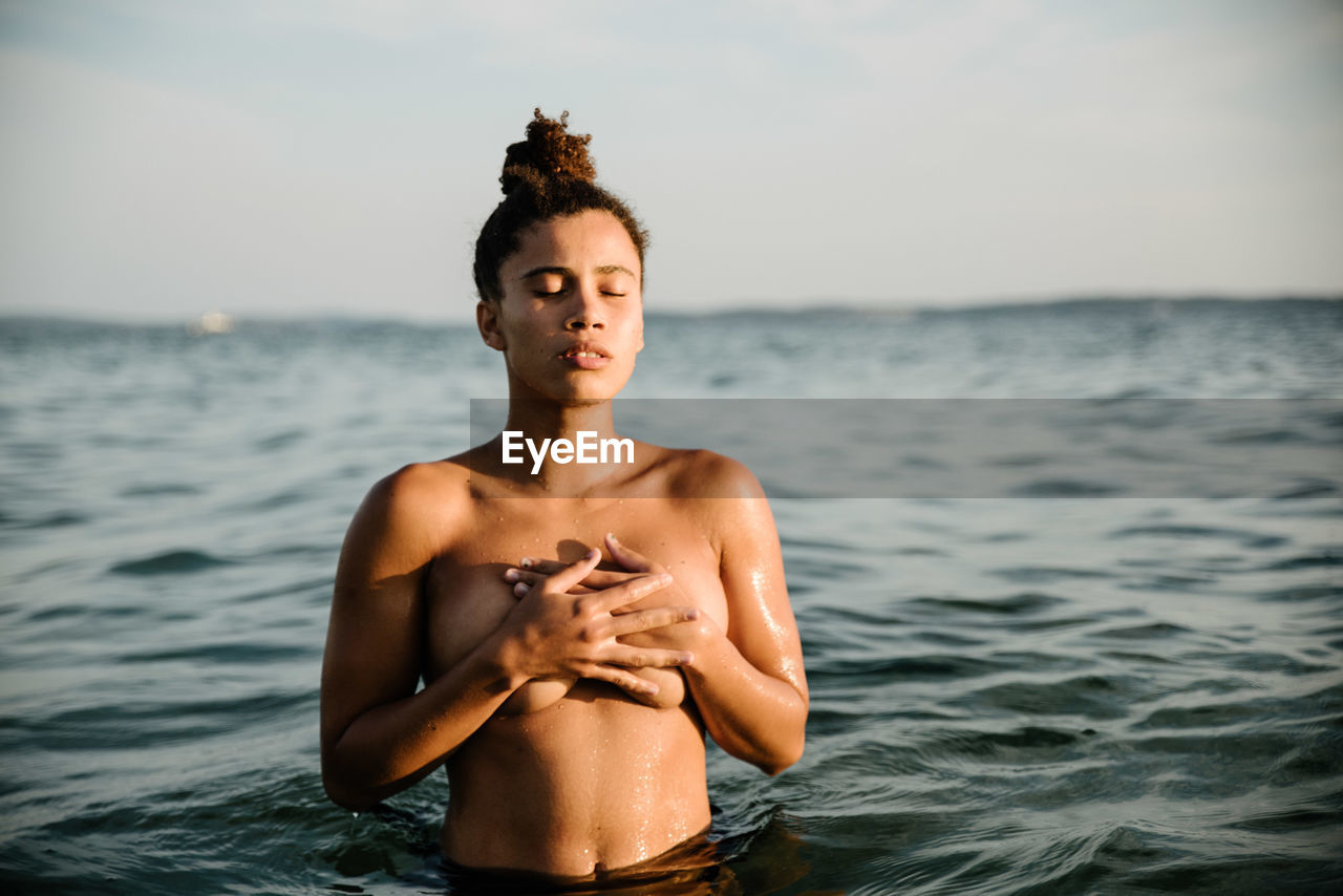 Shirtless young woman swimming in sea against sky