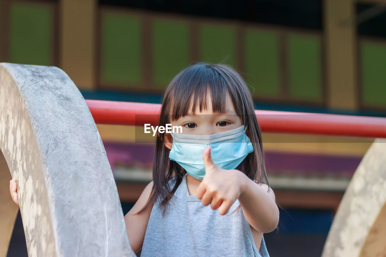 Portrait of girl wearing mask gesturing at playground