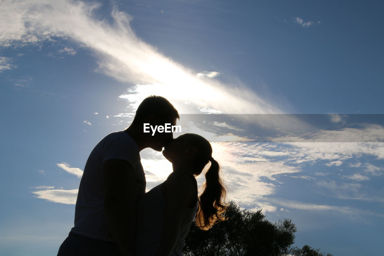 Low angle view of man and woman kissing against sky on sunny day
