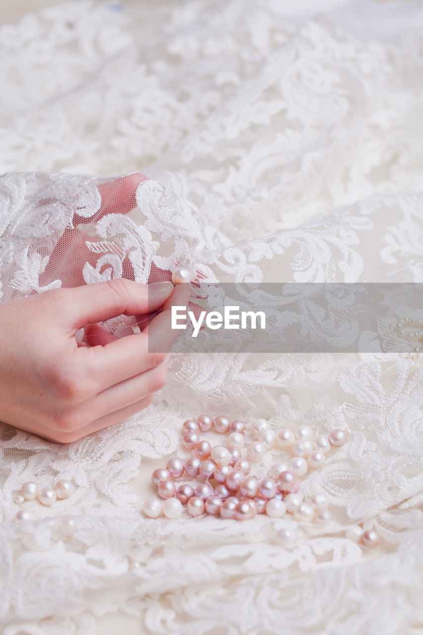 Cropped hand of woman stitching pearls on white wedding dress