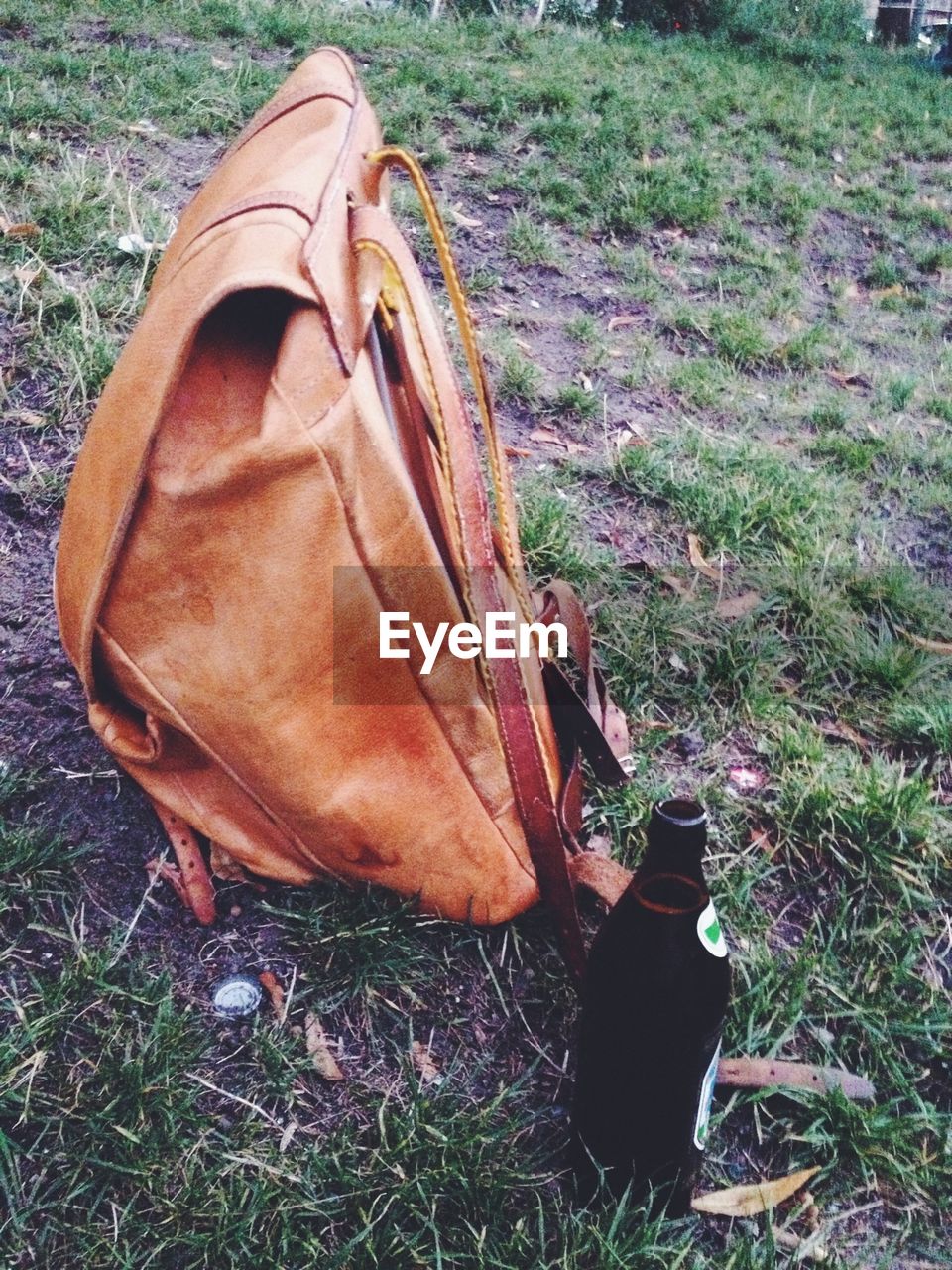Leather backpack and beer bottle on field