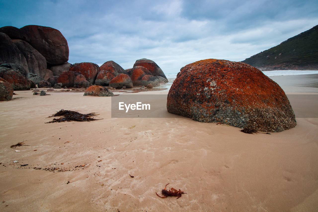 Rocks on sand at beach against sky