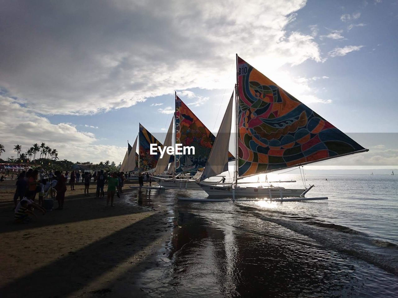 People and boats at beach against cloudy sky