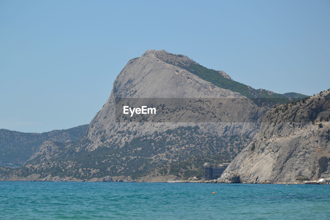 Scenic view of sea and mountains against clear blue sky