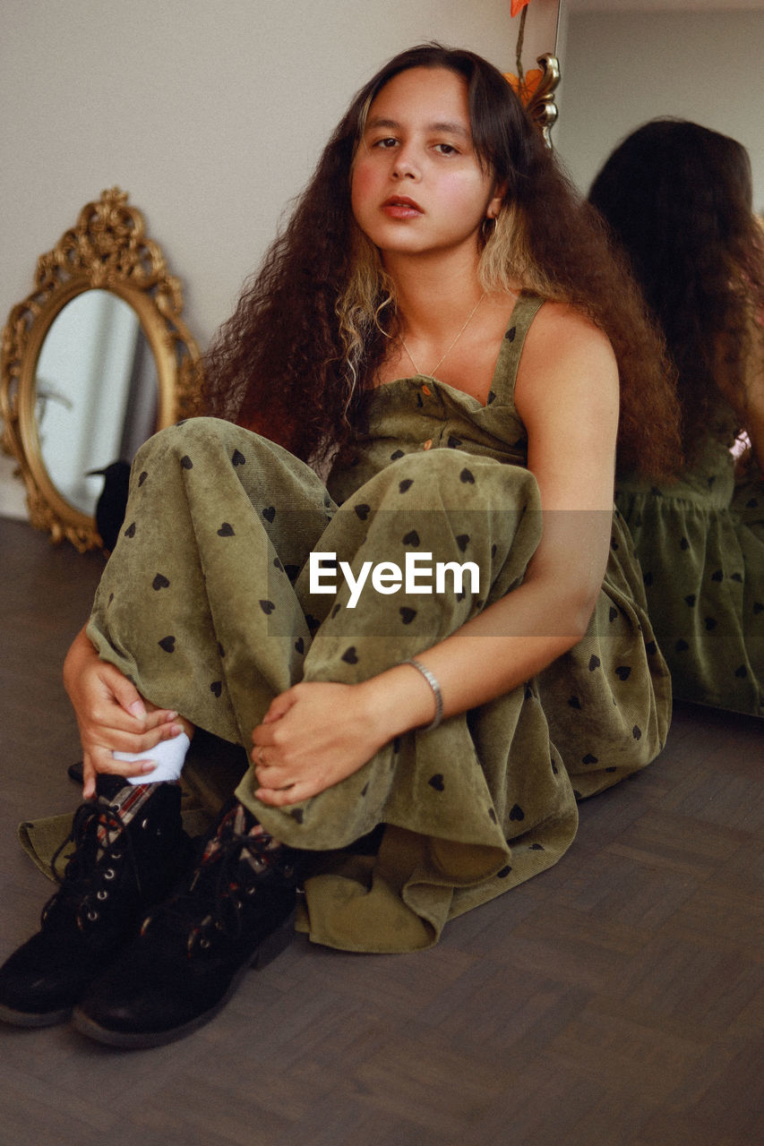 Portrait of young woman sitting on the floor at home in front of mirrors