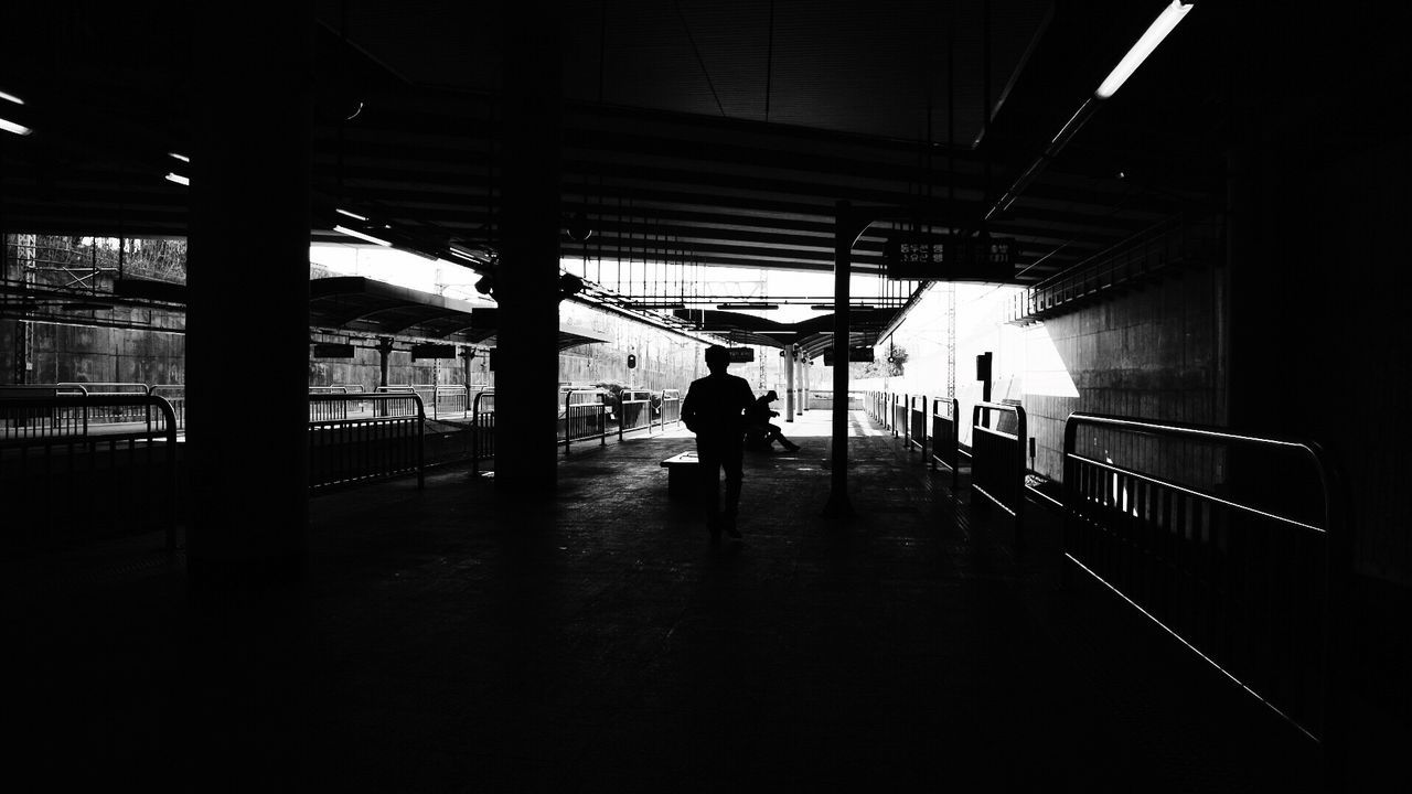 REAR VIEW OF MAN WALKING ON RAILROAD STATION