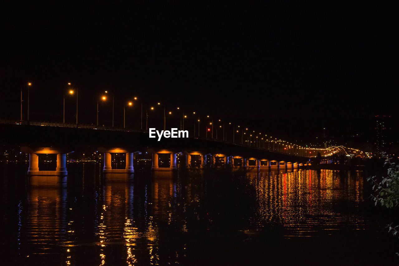 Illuminated bridge over river against sky at night