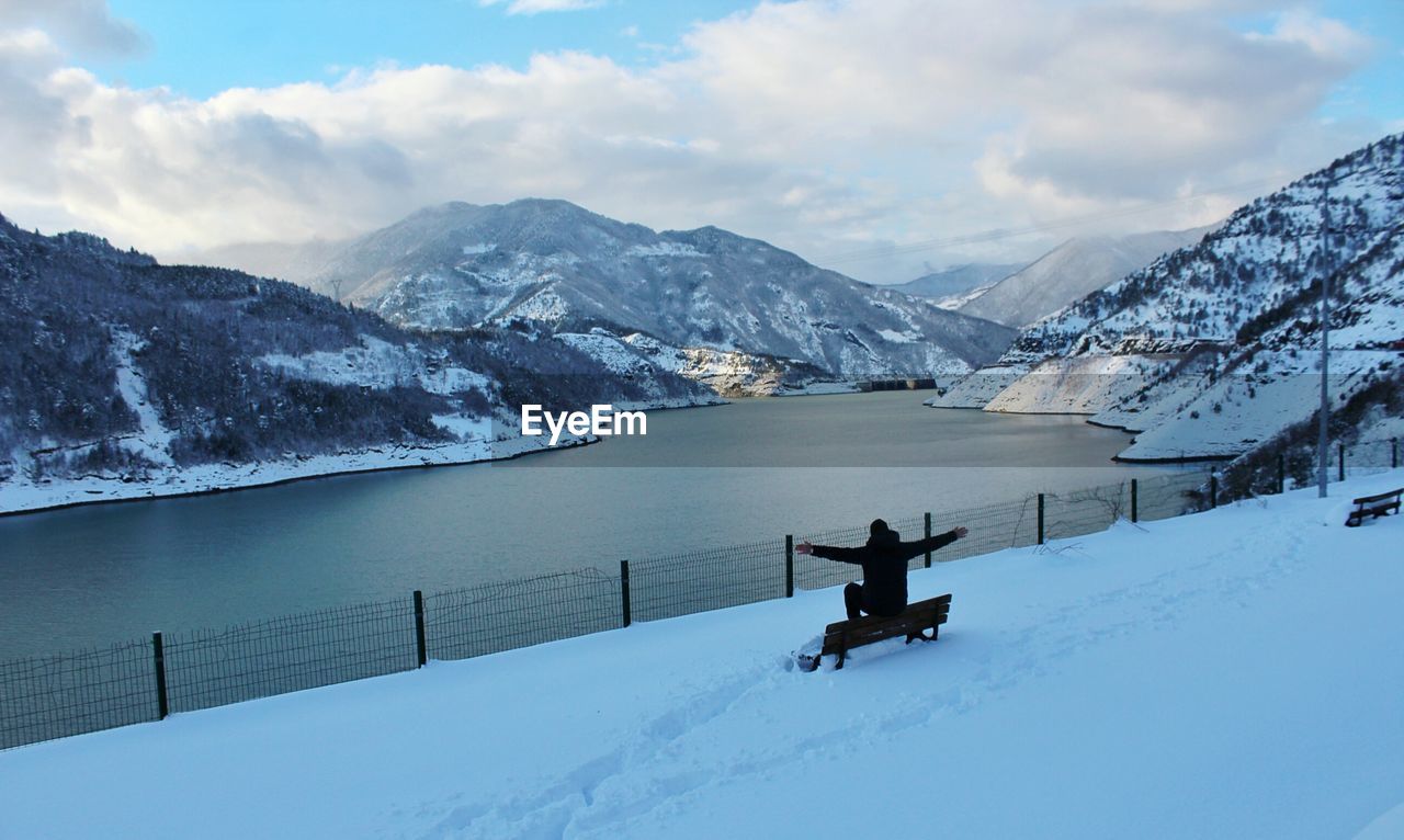 High angle view of man sitting with arms outstretched on bench during winter