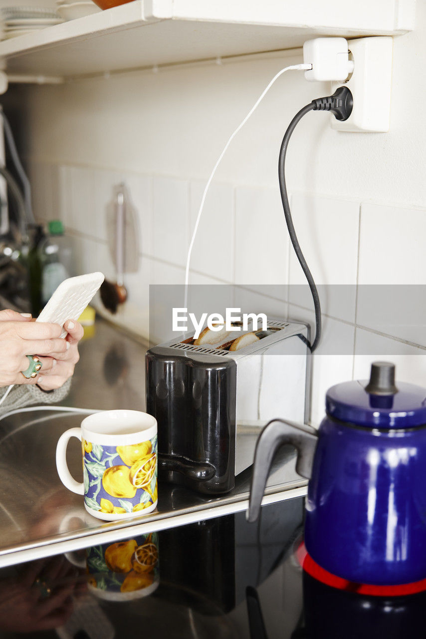 Hands holding cell phone over kitchen worktop