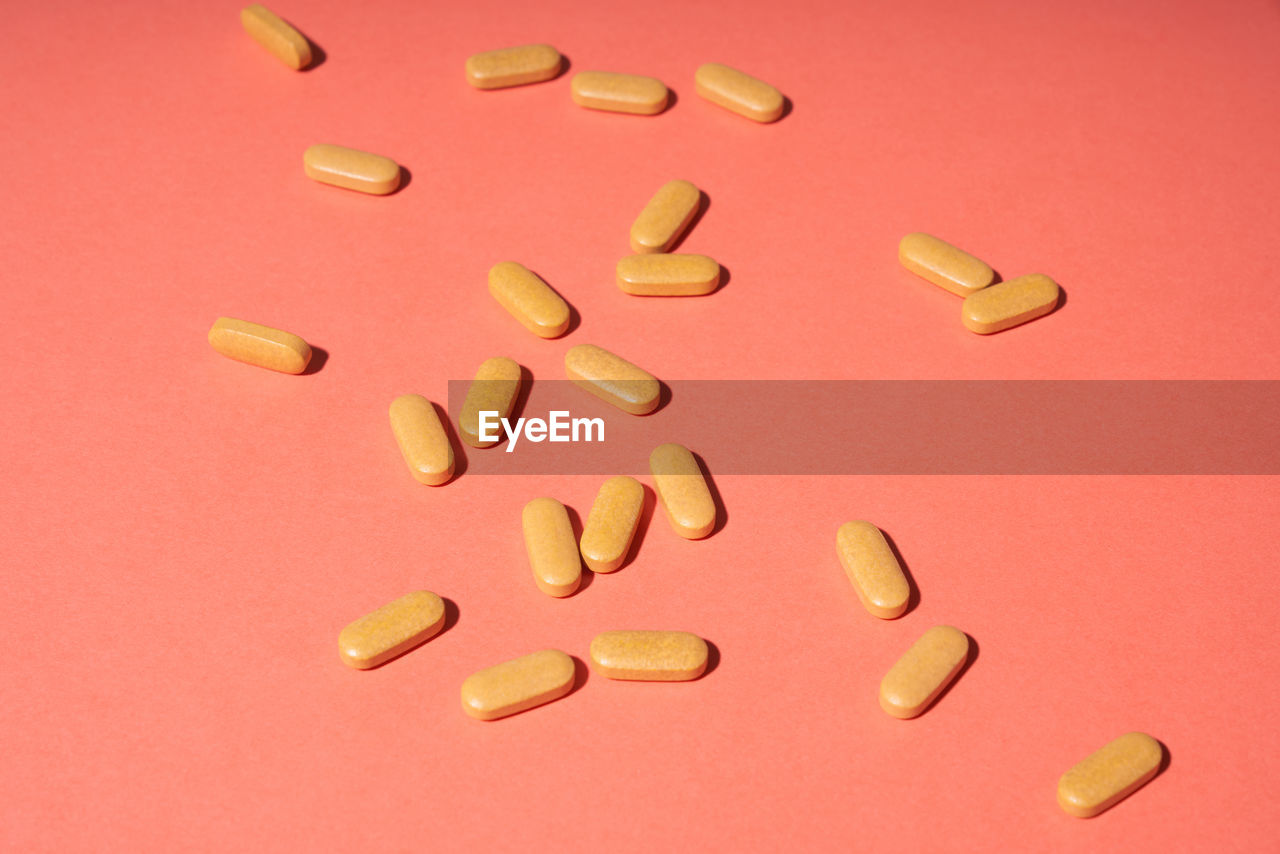 Few orange pills randomly on a pink background