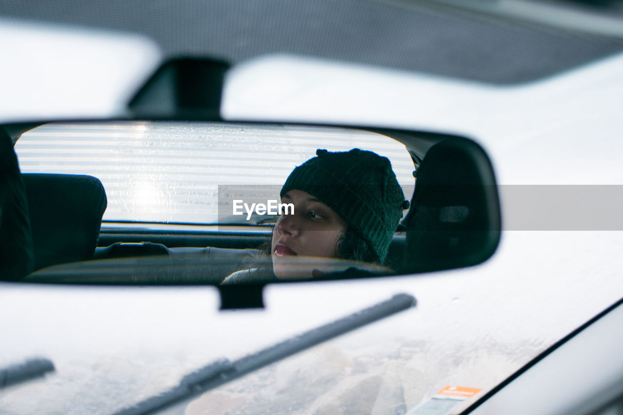 Reflection of young woman on rear-view car mirror