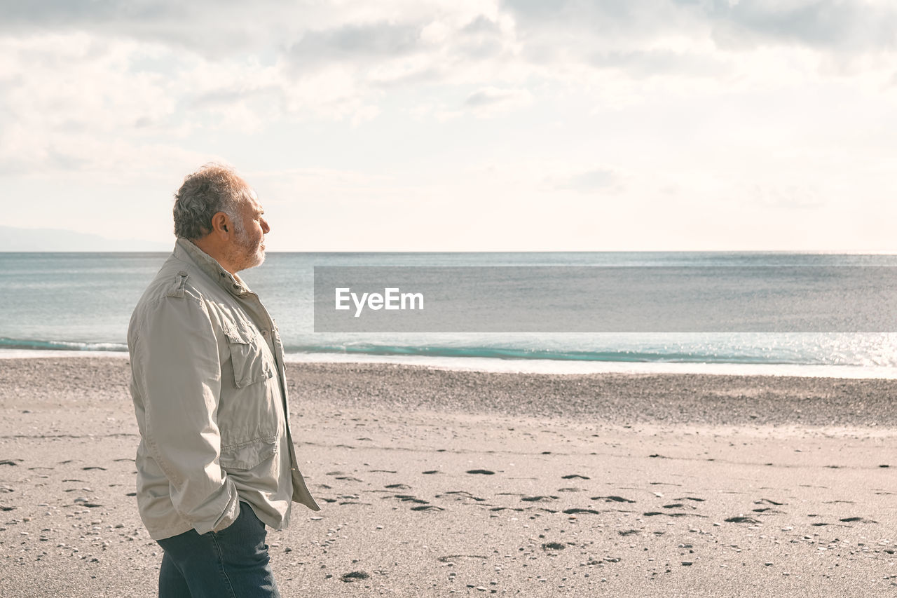 Happy middle-aged bearded man walking along deserted winter beach.