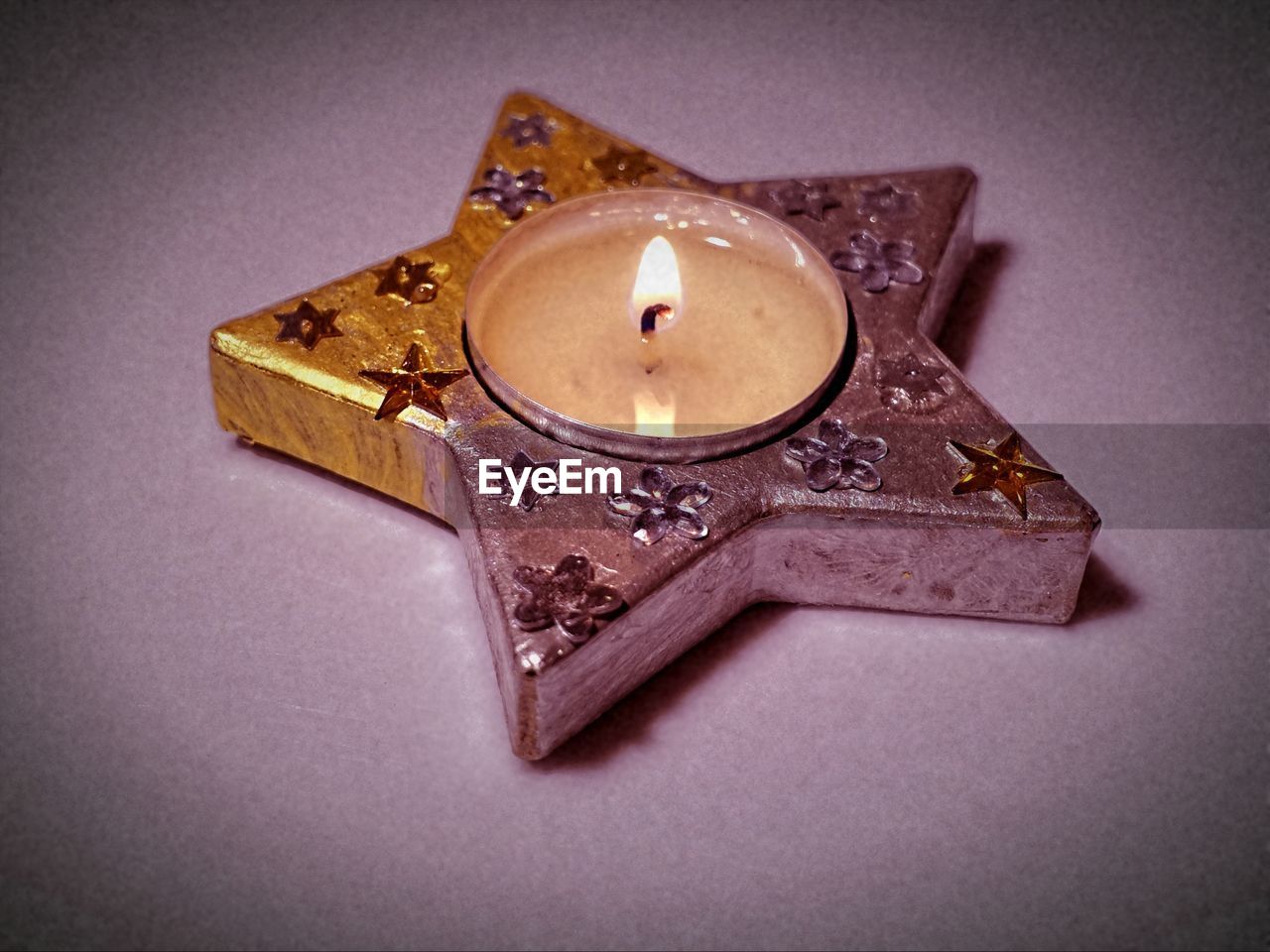 Close-up of star shape tea light candle on colored background