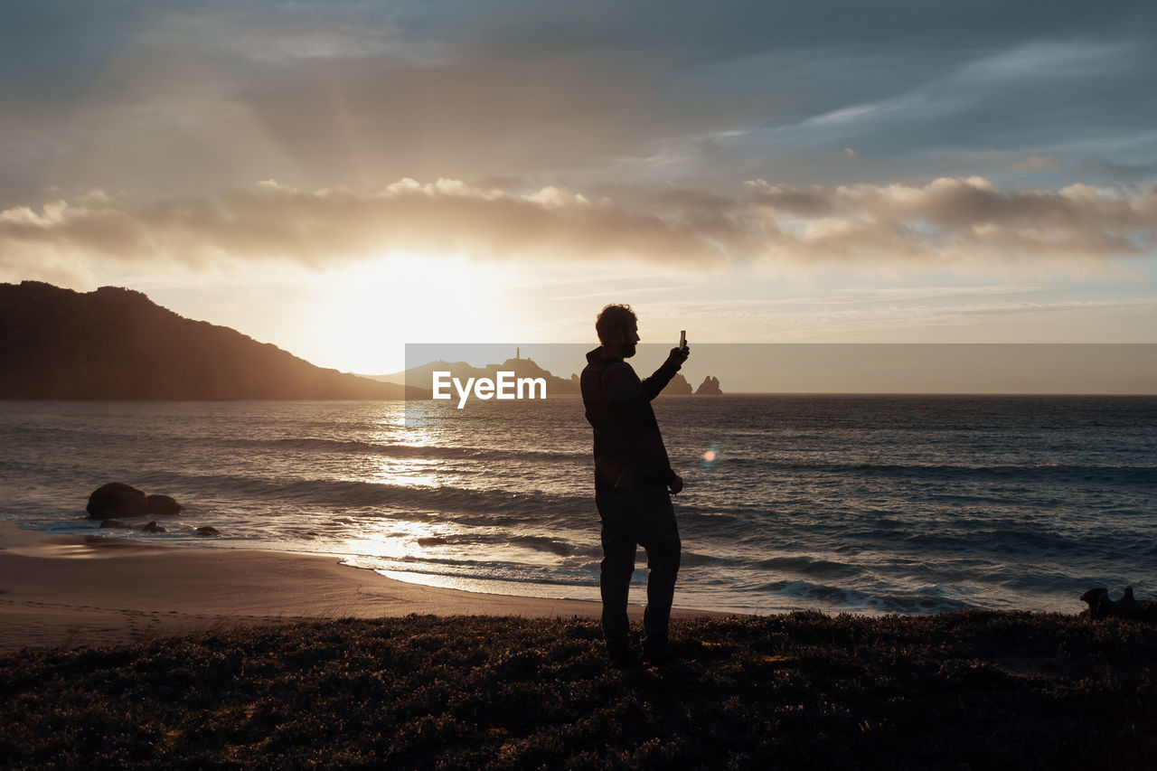 Man standing on beach against sky during sunset