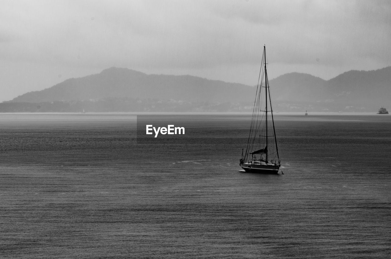 SAILBOAT SAILING ON SEA AGAINST MOUNTAIN RANGE