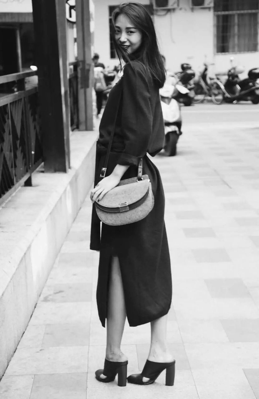 Portrait of smiling young woman with shoulder bag standing on street