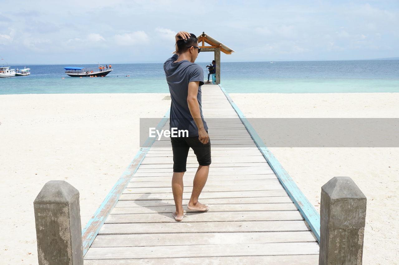 Rear view of man standing on beach against sky