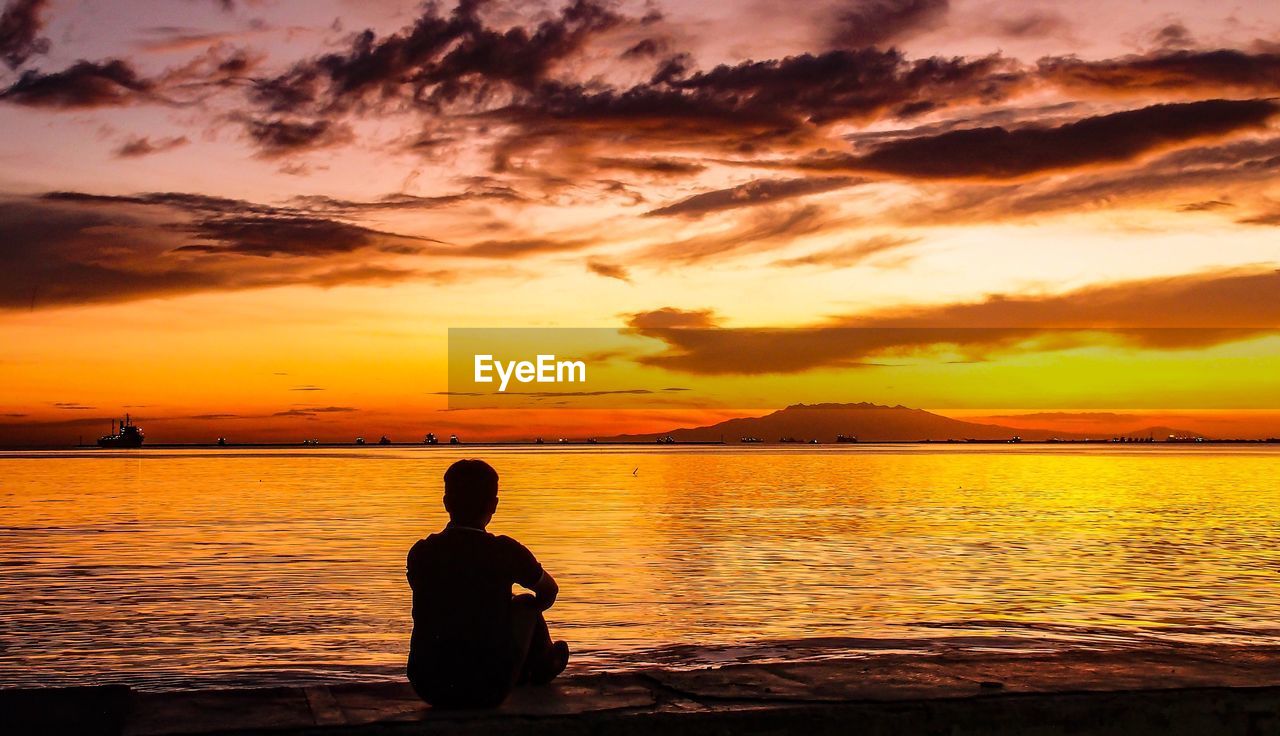 Silhouette man looking at sea against sky during sunset