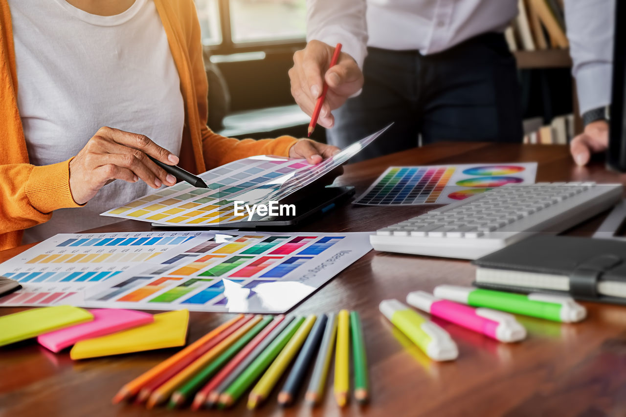 Midsection of creative occupation people pointing at color swatch sitting on table