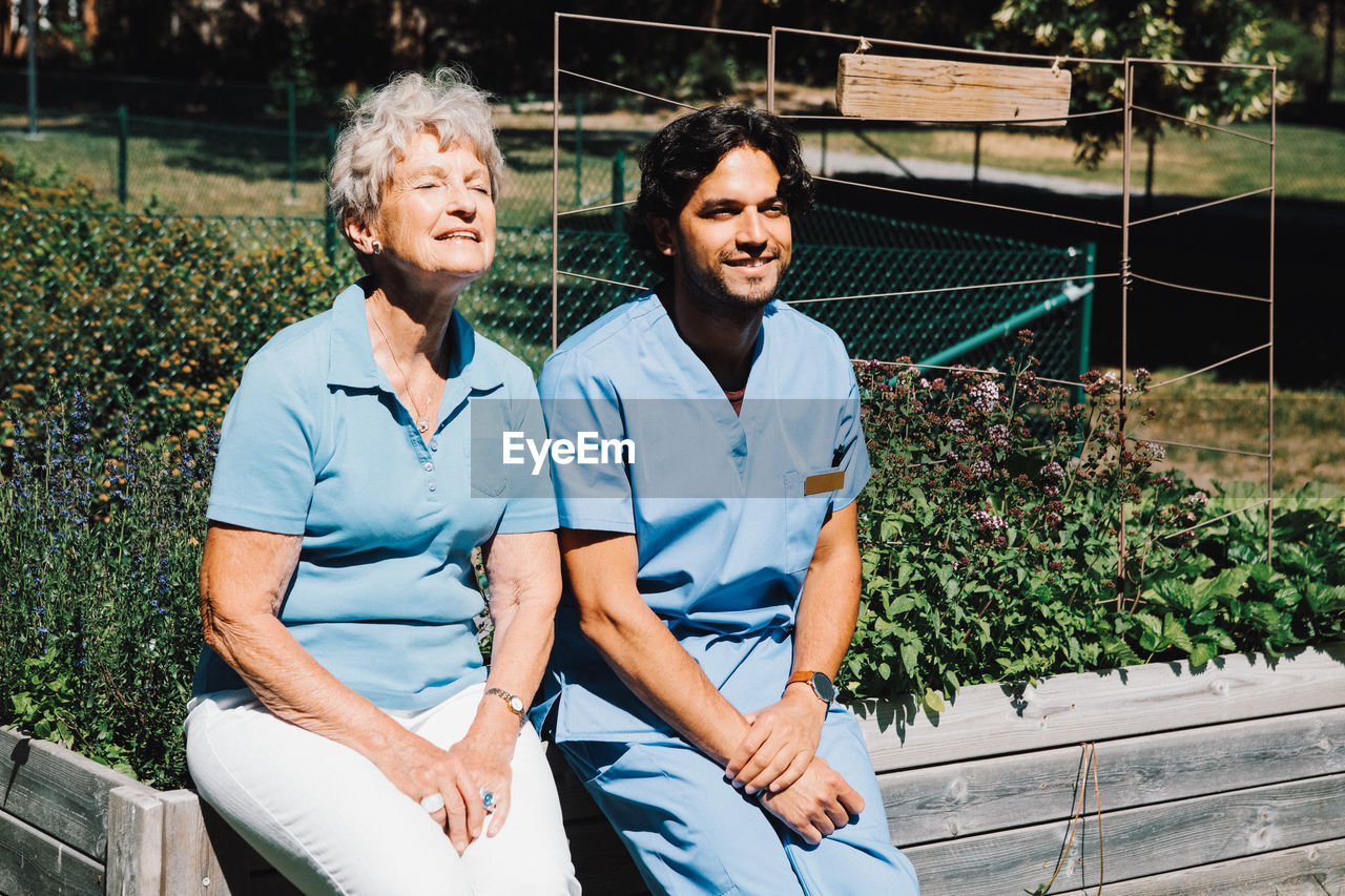 Smiling senior woman sitting with male nurse on planter at back yard