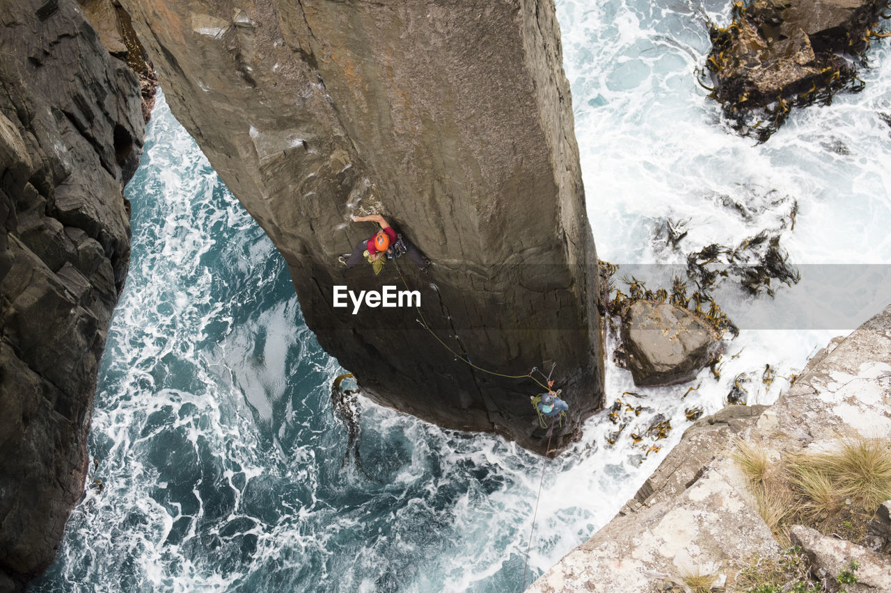 Rock climber chalks up as he climbs the totem pole out of the ocean in cape hauy, tasman national park, tasmania, australia.