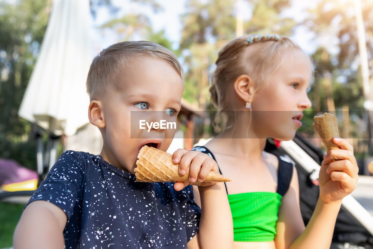 Cute sibling eating ice cream while sitting outdoors