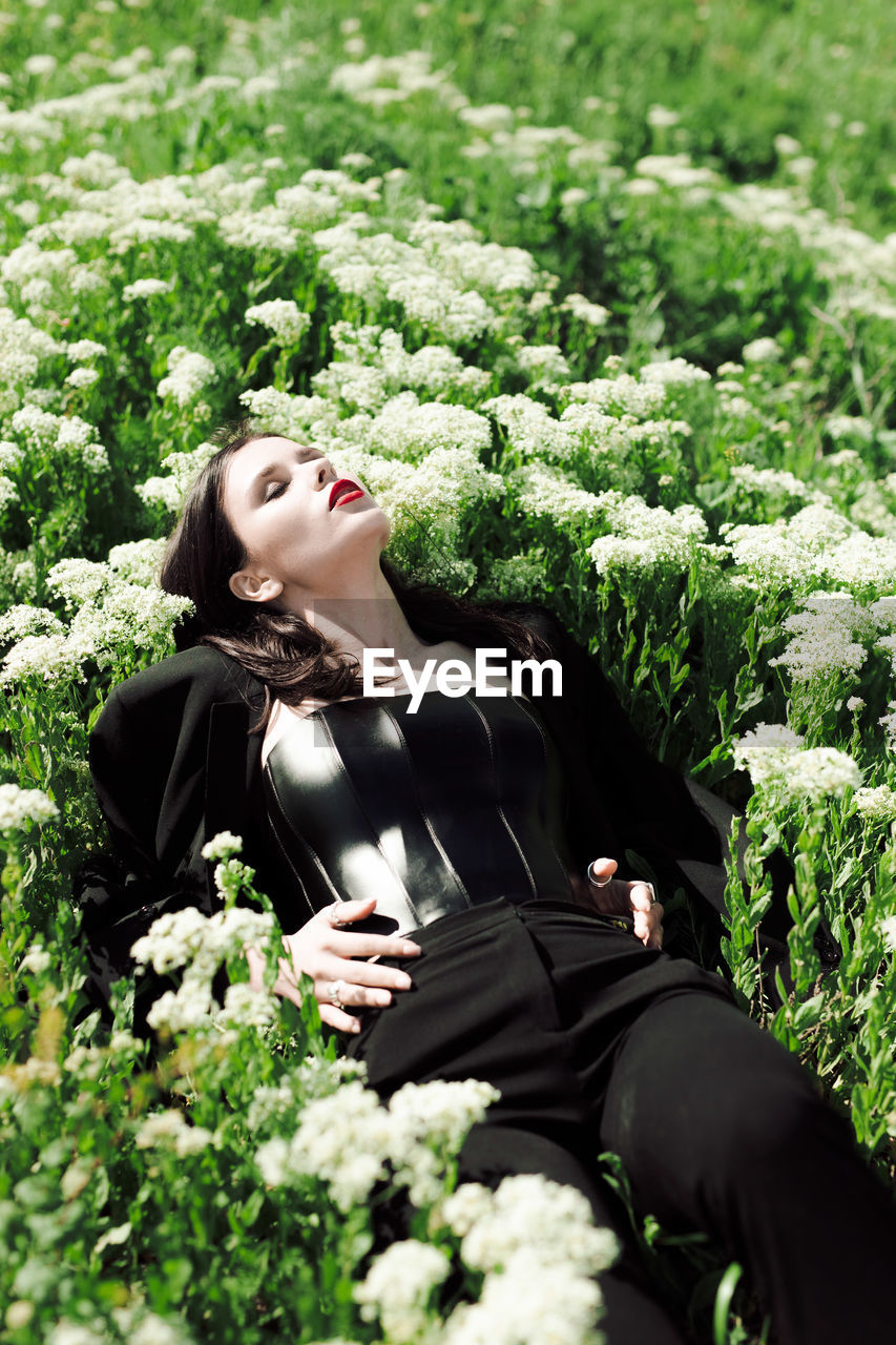 Girl model in black outfit laying on white flowers in field