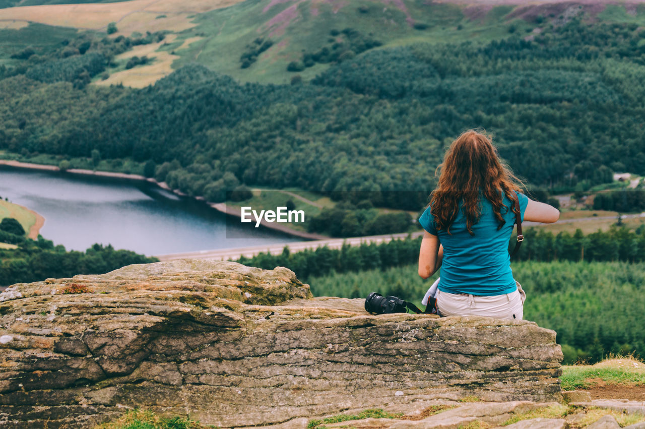 Rear view of woman sitting on rock by lake