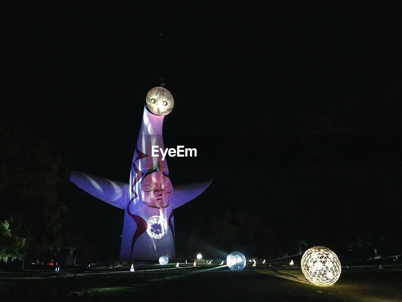 MAN STANDING AGAINST ILLUMINATED FERRIS WHEEL AT NIGHT