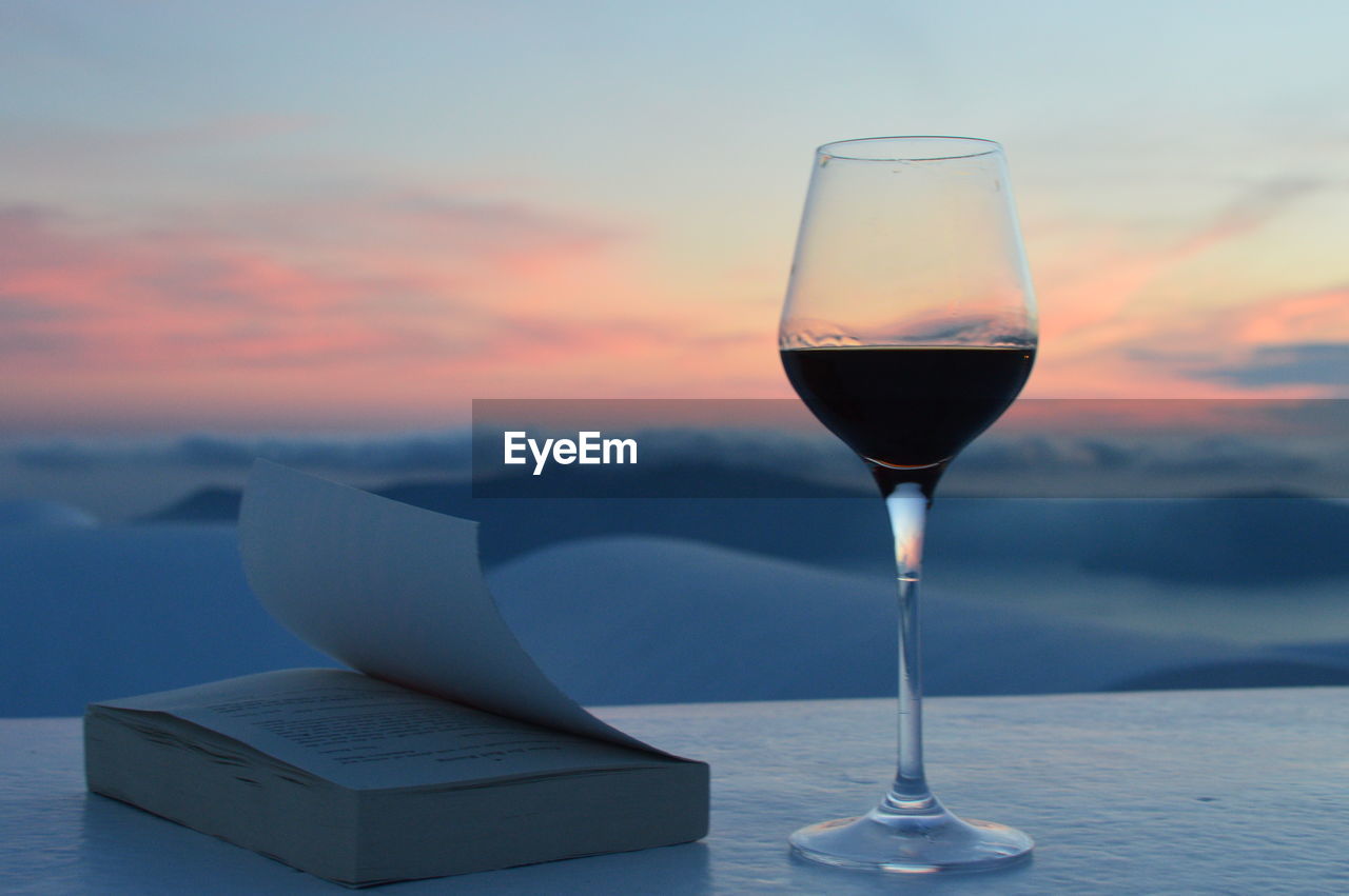 Wineglass with book on table against sky during sunset