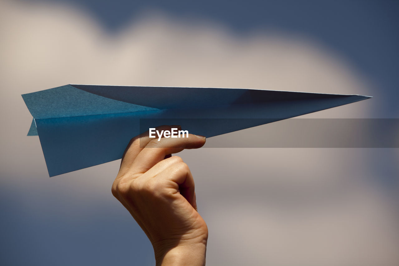 Cropped hand of woman holding paper airplane against sky