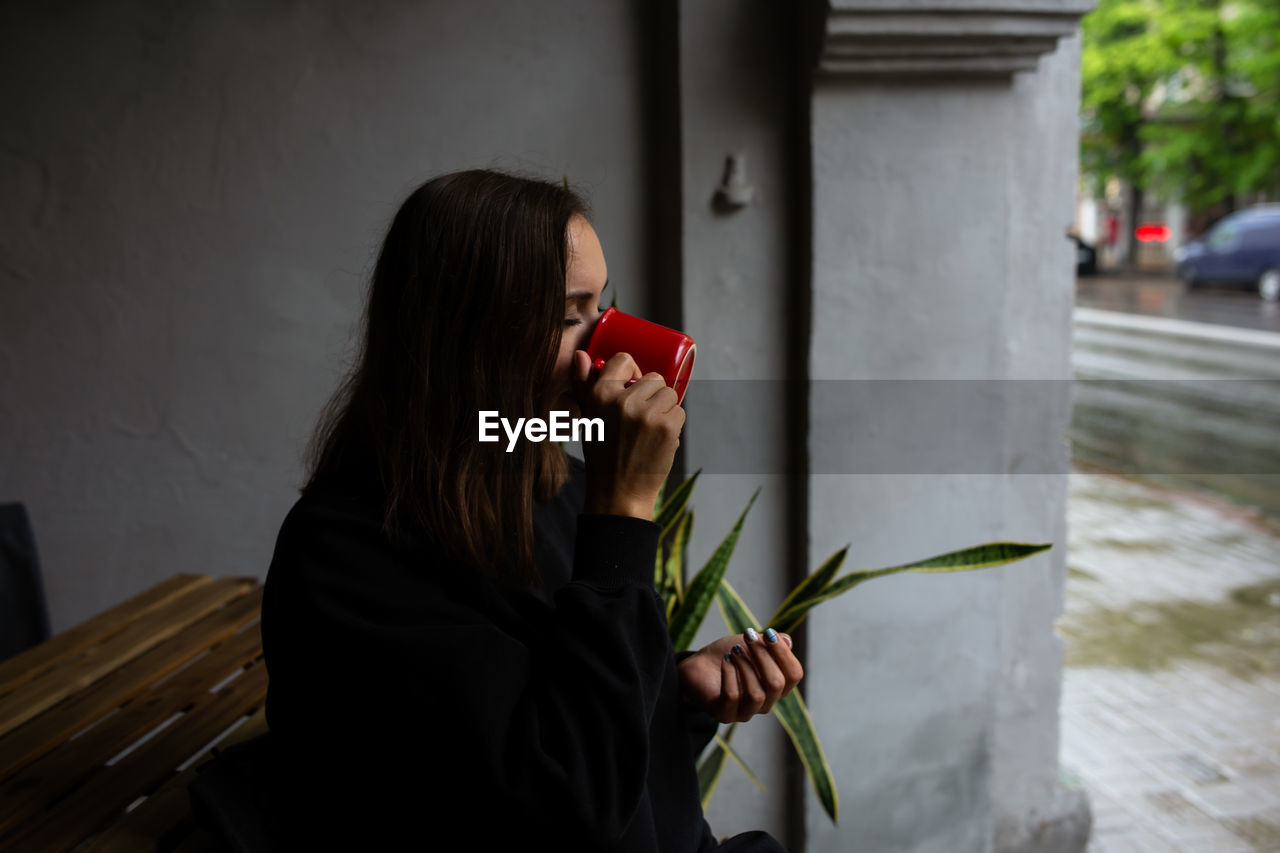 Young woman alone drinking a drink in a terrace cafe on a rainy day