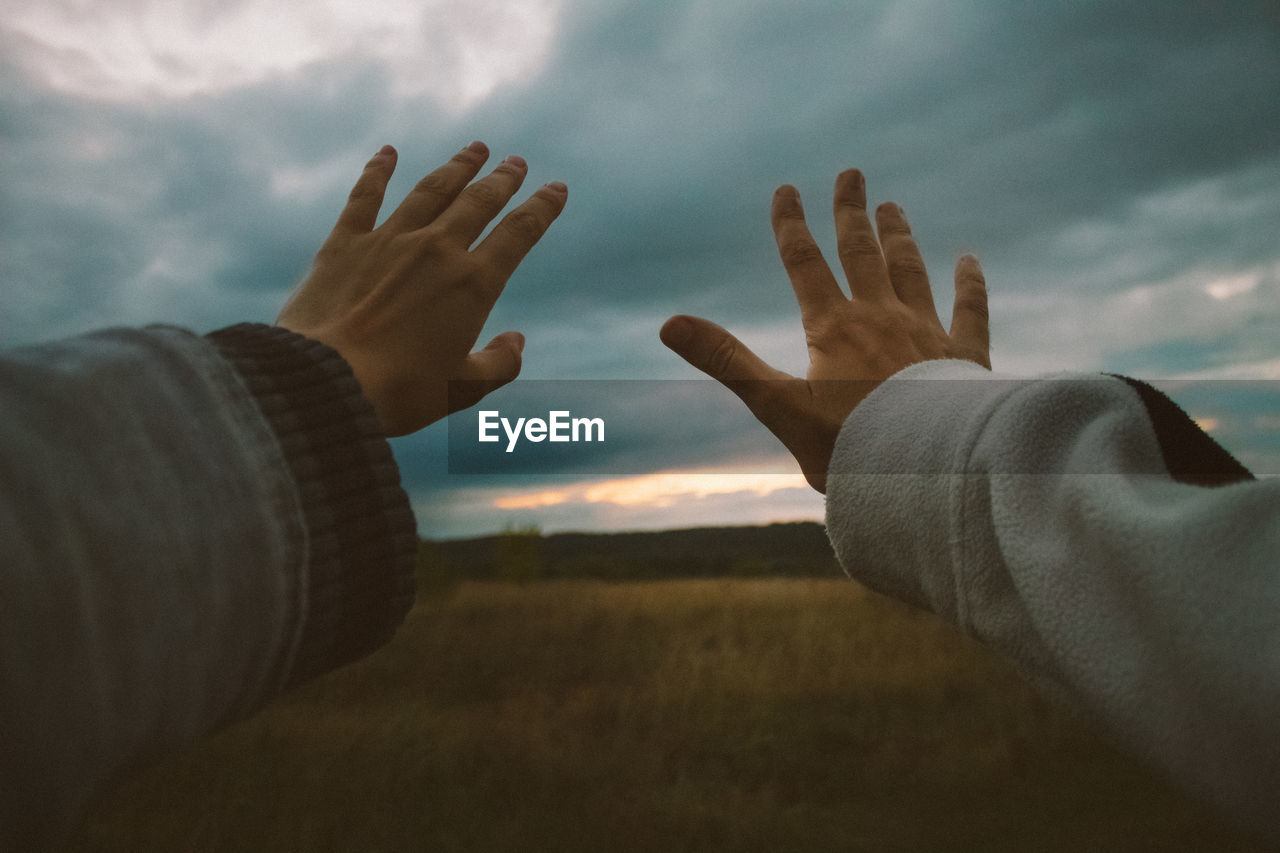 Cropped image of hands against cloudy sky