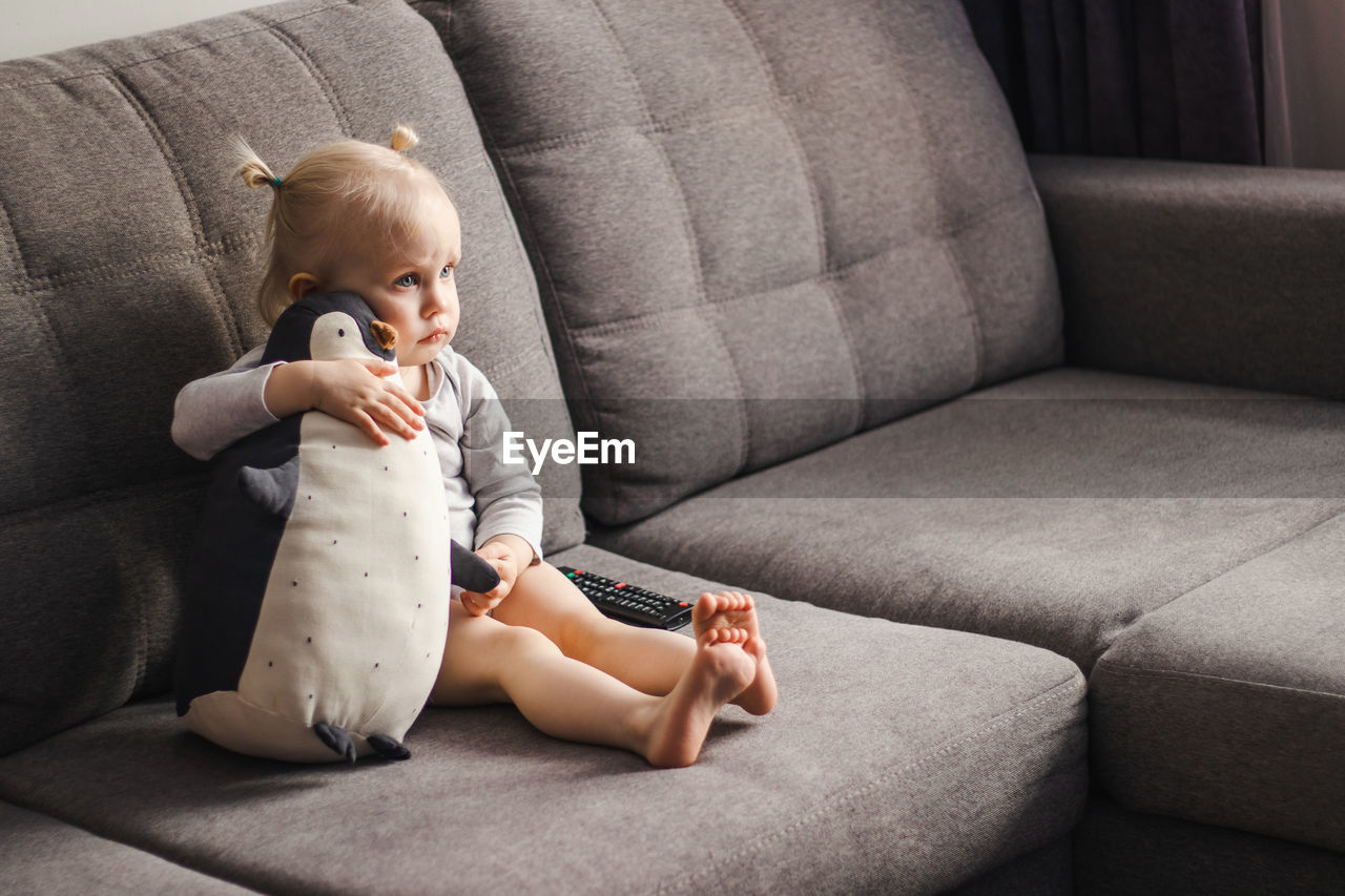 Little girl hugging a toy penguin on the couch
