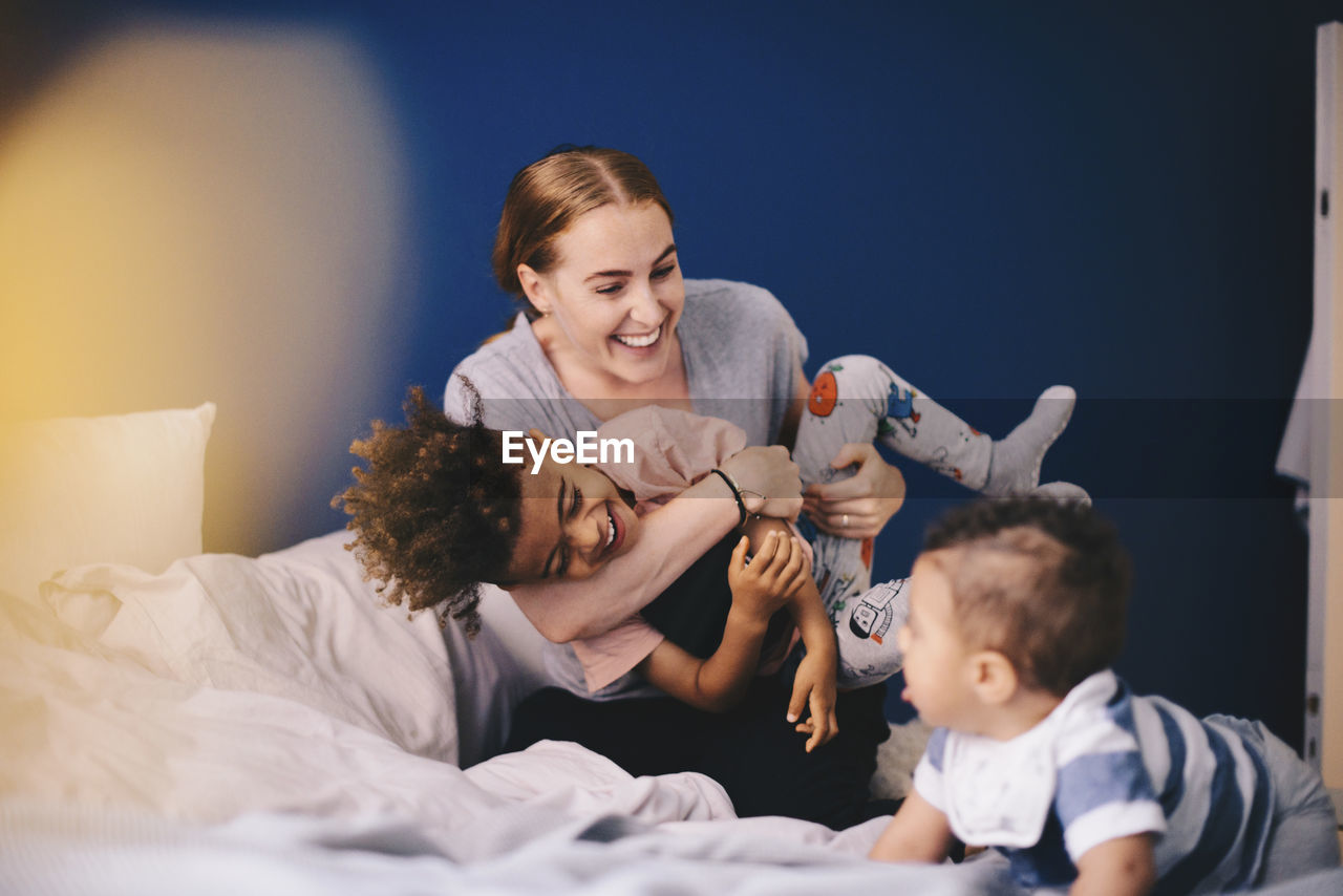 Smiling mother playing with children on bed at home