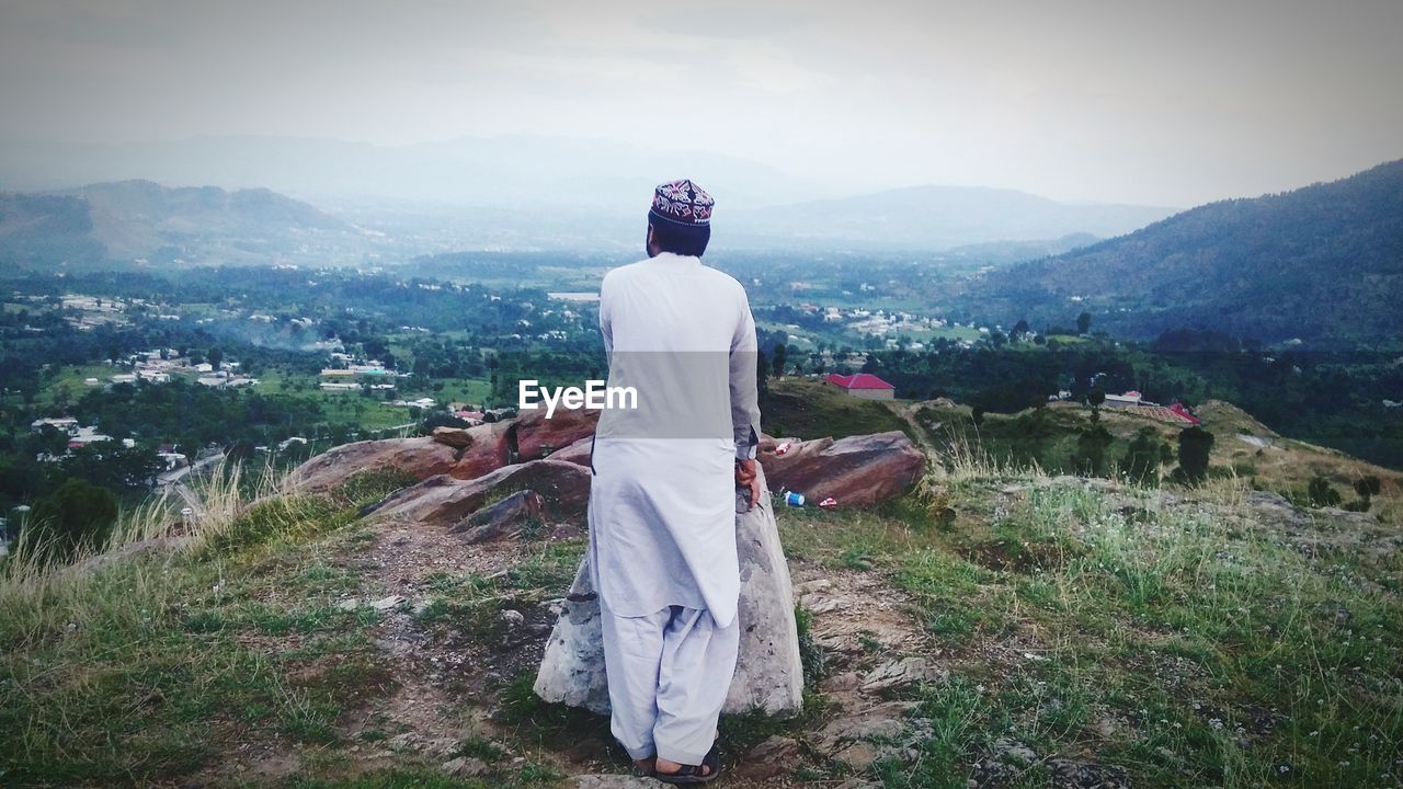 REAR VIEW OF WOMAN ON LANDSCAPE AGAINST MOUNTAIN